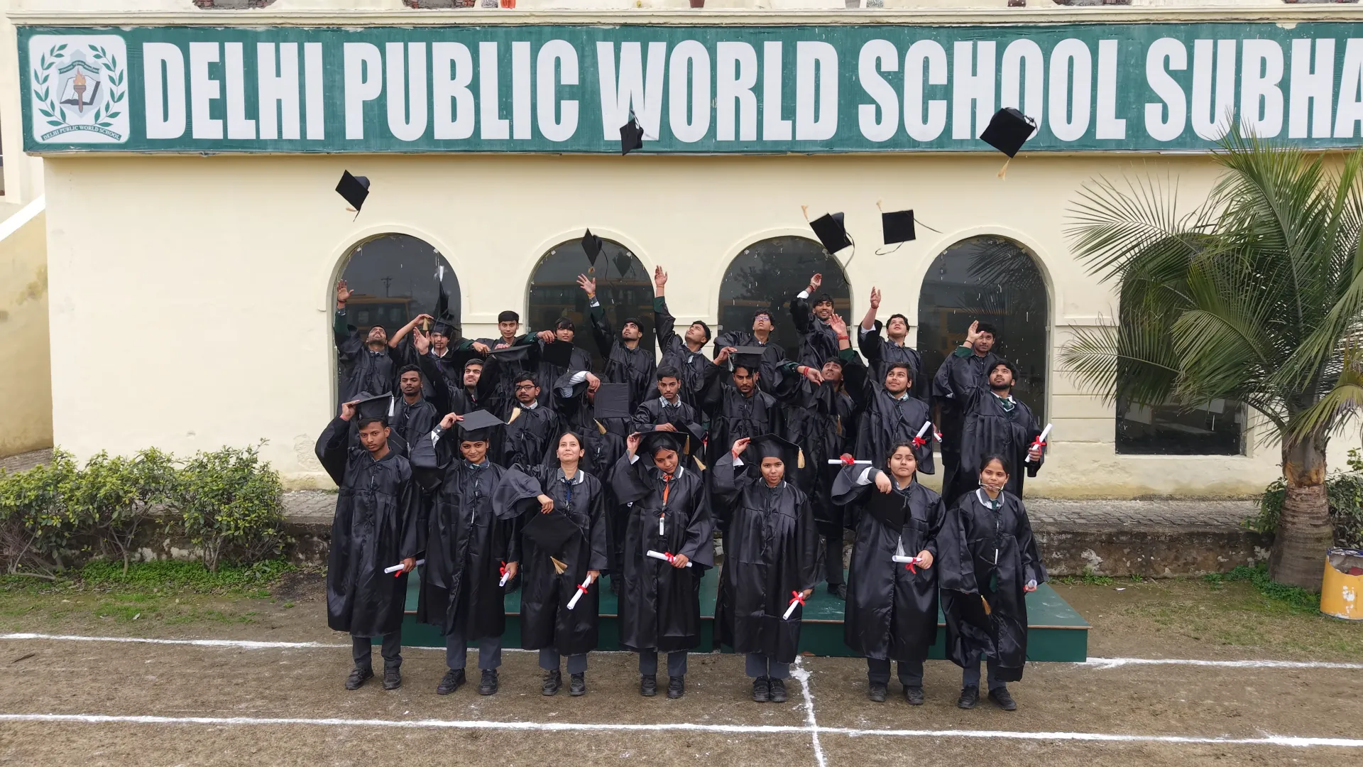 Class XII graduates in caps and gowns in front of the school building
